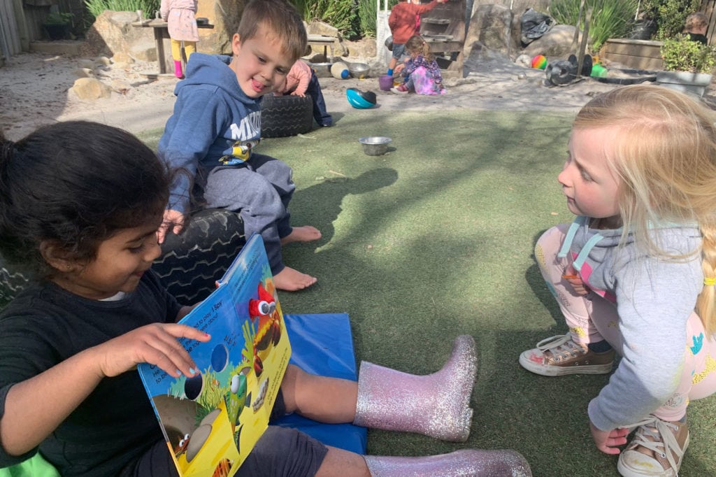Children reading a book outside Early Learning Centre